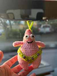 a person holding a crocheted pink spongebob toy in a car